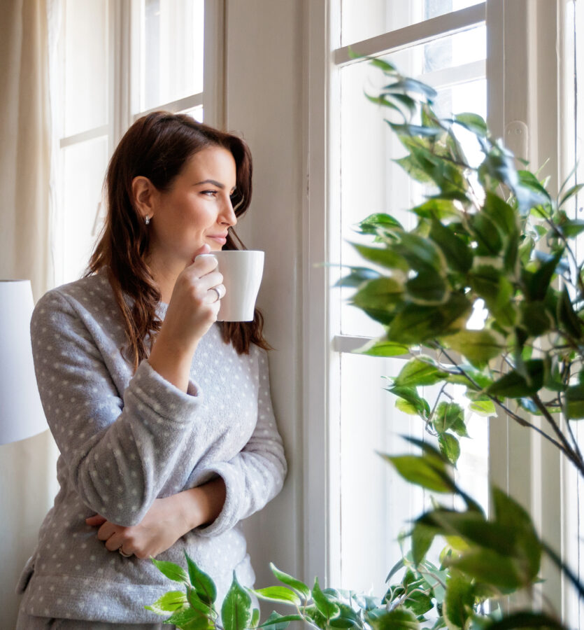 Woman at home drinking coffee and enjoying lake views from window
