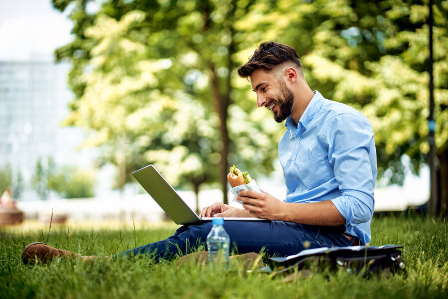 Young professional man enjoying lunch in the park with his laptop near corporate campus